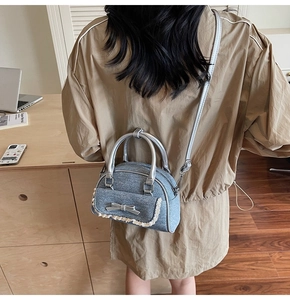 Detail of light blue textured ballet-style shell bag with silver bow and lace trim