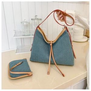 Detail view of denim hobo bag and small pouch set with tan leather trim and red edges