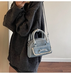 Detail of light blue denim shell bag with white lace trim and bow accent for women