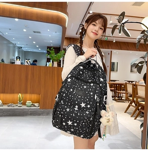 Lifestyle view of black star print backpack with white plush bunny charm in cozy cafe