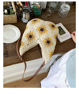 Detailed view of hand-crocheted sunflower hobo bag with brown leather strap on wooden table
