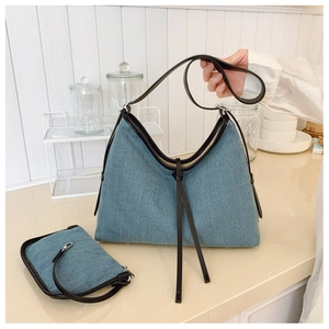 Detail of blue denim tote bag with black leather trim and decorative long fringes