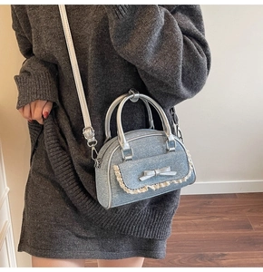 Detail of light blue denim shell bag featuring beige lace trim and silver bow accents