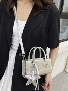 Silver glossy crossbody bag with star charm and metallic chain strap on model