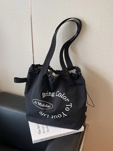 Minimalist black nylon tote bag with drawstring closure and artistic white lettering
