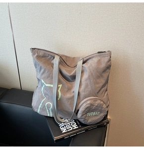 Foldable grey nylon tote bag with green cat detail and round coin purse on a sofa