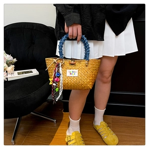 Close-up of woven straw beach bag with denim-wrapped handle and colorful star charms