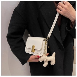 Detail of white mini crossbody bag with gold buckle and cute cream puppy leather charm