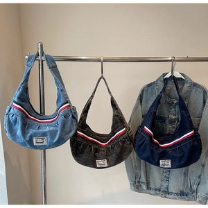 Close-up of three denim hobo bags in light blue, gray, and dark blue on metal rack