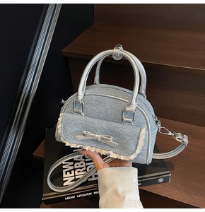 Detail of light blue denim shell bag with lace trim and silver faux leather handles