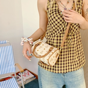 Detail of a beige cylinder crossbody bag with cartoon bear and vintage monogram texture