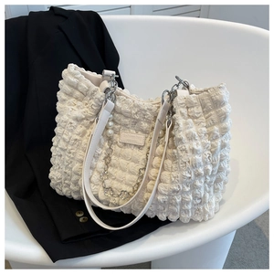 Close-up of beige quilted tote bag featuring pearl chain and fashion label on a chair