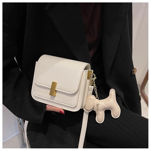 Detailed view of white leather crossbody bag with gold buckle and a cute dog charm accessory