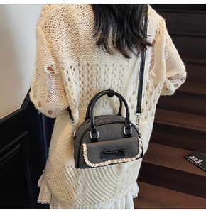 Detail of dark grey ballet-style shell bag with black bow and white lace trim detail