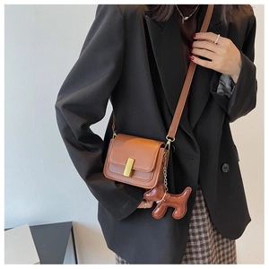 Detailed view of a brown leather shoulder bag featuring a golden buckle and dog pendant