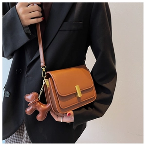 Detail of brown faux leather crossbody bag featuring gold buckle and cute puppy charm