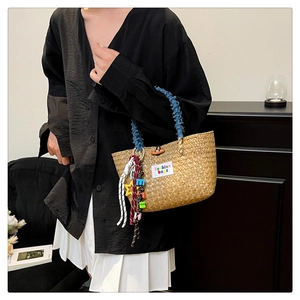 Detail of handwoven straw bucket bag with blue denim handles and colorful charms