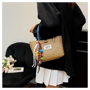 Detail of handmade straw beach bag featuring colorful letter charms and woven tassels