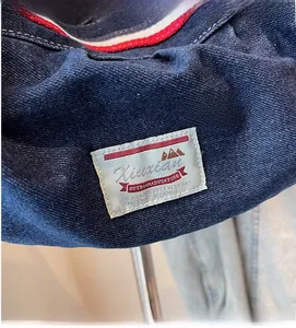 Close-up of a blue denim shoulder bag featuring a rustic outdoor adventure woven label