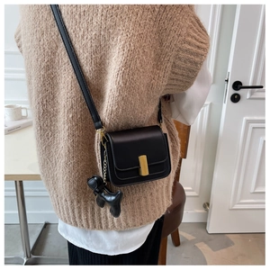Detail of a black leather crossbody bag featuring a gold buckle and cute puppy pendant