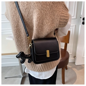 Close-up of black leather crossbody bag featuring gold buckle and cute puppy charm