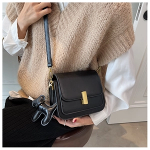Close-up of black crossbody bag with golden metal clasp and cute dog charm detail