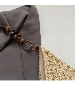 Macro detail of hand-woven straw tote with elegant wooden bead handle and metal ring