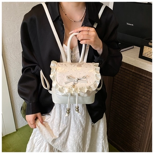 Close-up of cream white lace backpack with ruffle edges, bow detail, and pearl pendant