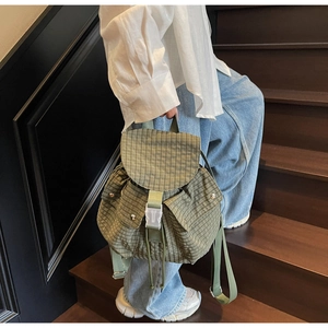 Detail eines grün-weiß karierten Segeltuch-Rucksacks mit transparenter Schnalle auf Holzstufen