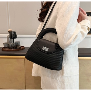 Detail of a black pleated leather handbag with silver lock worn by a model in a white blazer