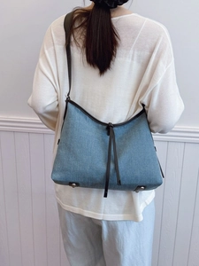 Denim hobo tote bag with brown leather trim and metal feet on white background
