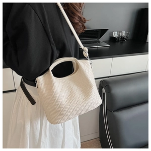 Detail of a beige woven bucket bag with circular handle and adjustable shoulder strap