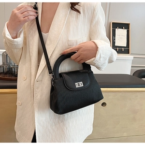Detail of black pleated bucket bag with silver twist lock and crossbody strap on a model