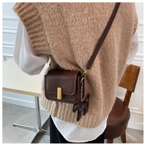 Detail of a brown leather crossbody bag with a cute rabbit charm and gold buckle