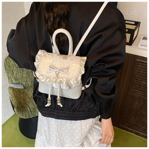 Detail of off-white ballet style mini backpack with lace edges and a bow pendant