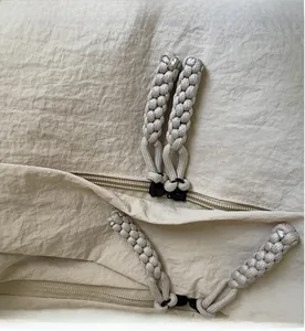 Detail of parcord woven zipper pull on beige nylon crossbody bag with textured fabric
