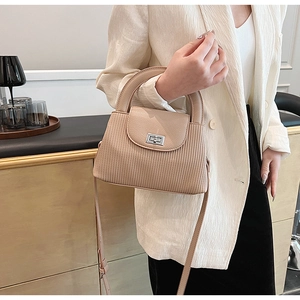 Detailed shot of beige pleated handbag with silver metallic square lock on beige blazer