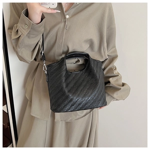 Detail of black woven tote bag featuring herringbone texture and silver metal hardware