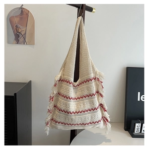 Detail of beige knitted tote bag featuring red wave patterns and fringe hanging on a hanger