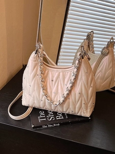 Beige gesteppte Umhängetasche mit Strass und Silberkette auf einer schwarzen Holzfläche