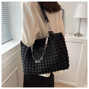 Detailed close-up of a black quilted tote bag with pearl chain and flower charm detail