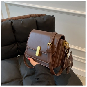Detail of dark brown leather crossbody bag with gold buckle and side bow charm
