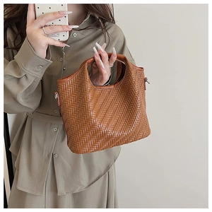 Detailed view of brown woven bucket bag with metal side buckles and sturdy leather handle