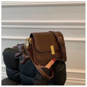 Detail of dark brown crossbody bag with matte gold lock and cute bear charm pendant