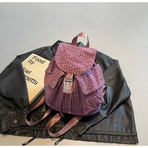Detail eines lila karierten Rucksacks mit weißem Schnallenverschluss auf schwarzem Leder