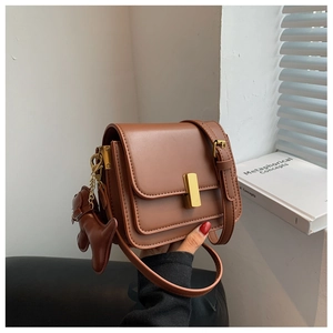 Detail of a brown leather shoulder bag with gold metal clasp and dog-shaped charm
