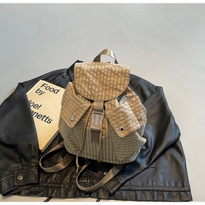 Detail eines beigen karierten Rucksacks mit Schnallen und Seitentaschen auf schwarzem Leder