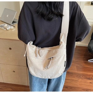 Close-up of beige crescent nylon bag with wide strap and woven knot zipper detail