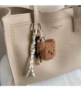 Close-up of a cute teddy bear charm with braided rope on a beige leather tote bag