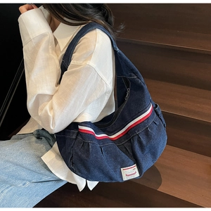 Detail of a dark blue denim crescent shoulder bag with red stripes and white brand tag